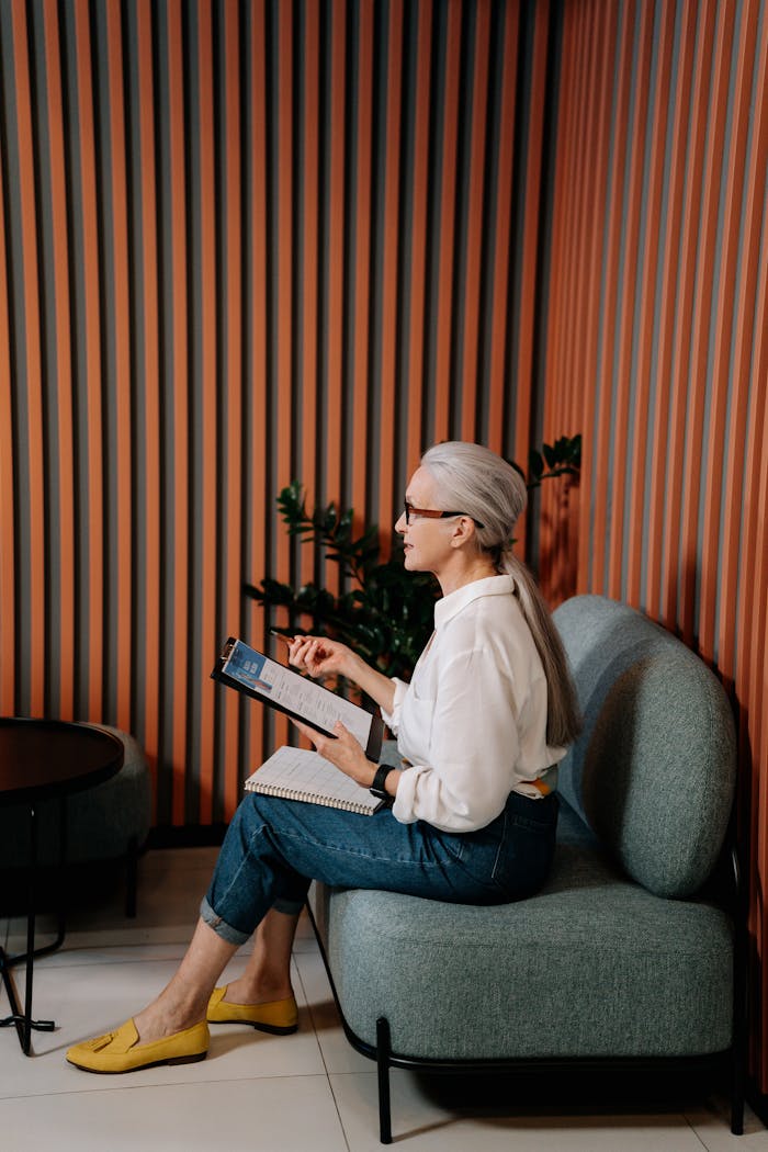 An adult woman in casual attire reviewing notes on a tablet in a stylish office setting.
